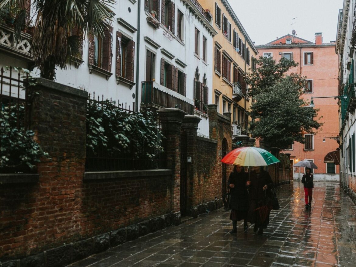 Menschen mit bunten Regenschirmen in einer regennassen Gasse
